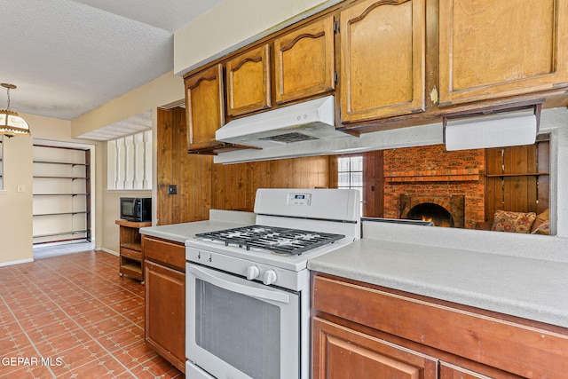 kitchen featuring white gas range, under cabinet range hood, light countertops, brown cabinetry, and a textured ceiling