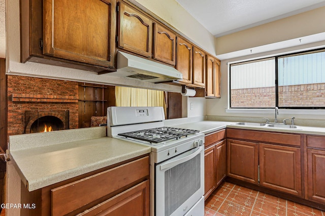 kitchen with gas range gas stove, under cabinet range hood, a sink, light countertops, and brown cabinets
