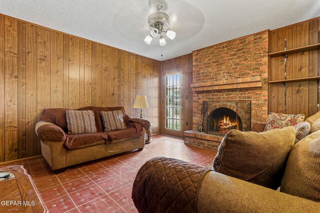 living area with ceiling fan, wood walls, a fireplace, and a textured ceiling