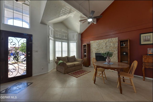 living area featuring high vaulted ceiling, ceiling fan, a fireplace, light tile patterned floors, and baseboards