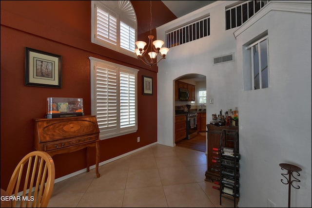 foyer entrance with arched walkways, a chandelier, a towering ceiling, light tile patterned floors, and baseboards