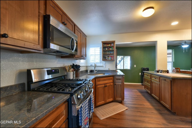 kitchen featuring appliances with stainless steel finishes, a sink, brown cabinets, dark wood-style flooring, and open shelves