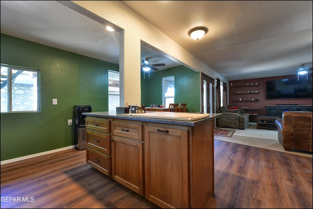 kitchen featuring dark wood-type flooring, open floor plan, ceiling fan, brown cabinets, and baseboards
