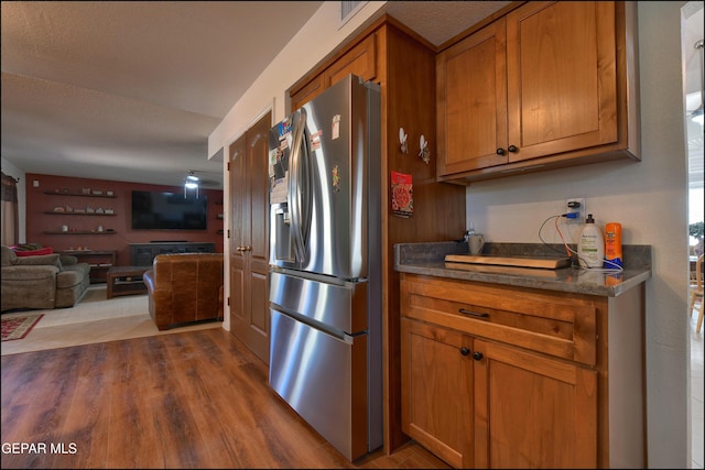 kitchen featuring stainless steel fridge with ice dispenser, brown cabinetry, dark countertops, dark wood-style flooring, and open floor plan