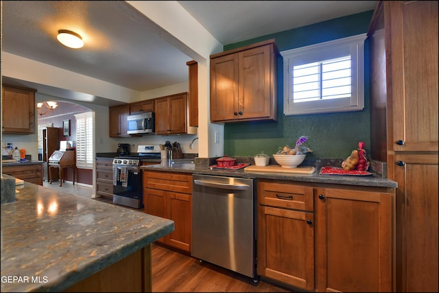 kitchen featuring appliances with stainless steel finishes, dark countertops, brown cabinets, wood finished floors, and a sink