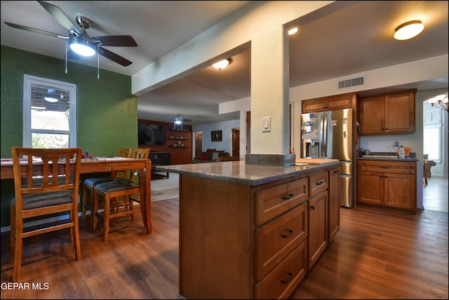 kitchen featuring dark wood finished floors, ceiling fan, brown cabinetry, stainless steel fridge, and a textured wall