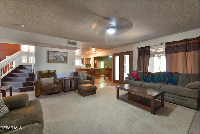 living room featuring stairs, ceiling fan, healthy amount of natural light, and a textured ceiling