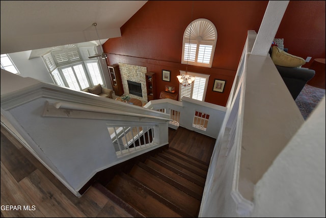 stairs with wood finished floors, ceiling fan, a chandelier, a fireplace, and vaulted ceiling