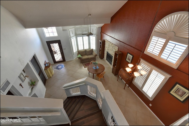 tiled living room featuring a towering ceiling, a fireplace, and ceiling fan