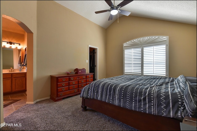 carpeted bedroom with arched walkways, a sink, ensuite bathroom, high vaulted ceiling, and a ceiling fan