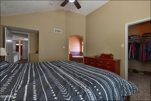 bedroom featuring arched walkways, a walk in closet, a closet, carpet floors, and high vaulted ceiling