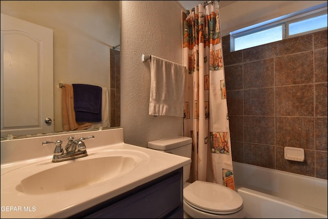 full bath featuring toilet, a textured wall, vanity, and shower / bath combo