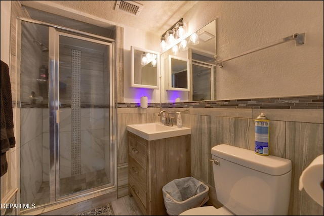 bathroom featuring tile walls, a shower stall, toilet, a textured wall, and vanity