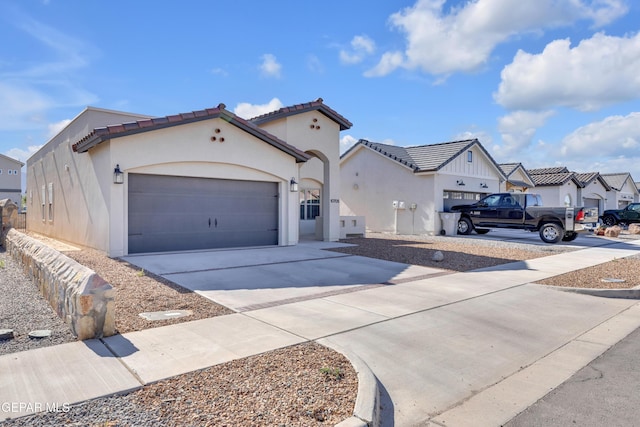 mediterranean / spanish house featuring concrete driveway, an attached garage, stucco siding, a tiled roof, and a residential view