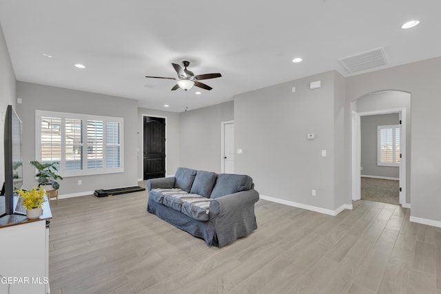 living area with arched walkways, light wood-type flooring, ceiling fan, baseboards, and recessed lighting