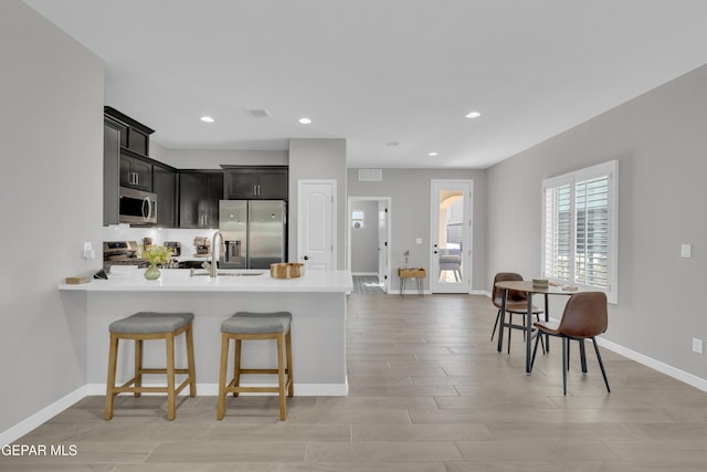 kitchen featuring stainless steel appliances, a peninsula, light countertops, baseboards, and a kitchen bar