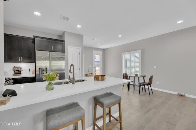 kitchen featuring stainless steel fridge with ice dispenser, a sink, a breakfast bar area, light countertops, and recessed lighting