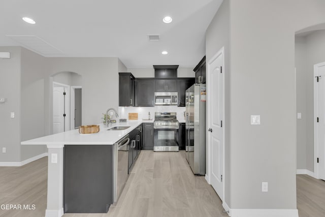 kitchen featuring stainless steel appliances, arched walkways, a sink, a peninsula, and light countertops