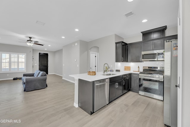 kitchen featuring appliances with stainless steel finishes, a sink, arched walkways, a peninsula, and baseboards