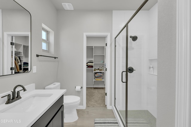 bathroom featuring a stall shower, a walk in closet, toilet, vanity, and baseboards