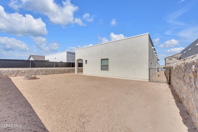 back of property featuring fence, stucco siding, and a gate