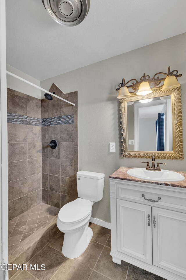 589 Gallagher St, El Paso, TX 79915 - full bathroom with a tile shower, toilet, vanity, tile patterned flooring, and baseboards