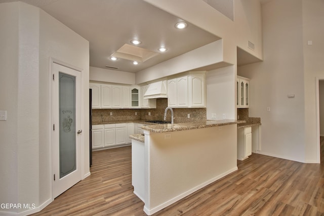 1483 Via Appia St, El Paso, TX 79912 - kitchen with custom range hood, a peninsula, glass insert cabinets, light wood-type flooring, and recessed lighting