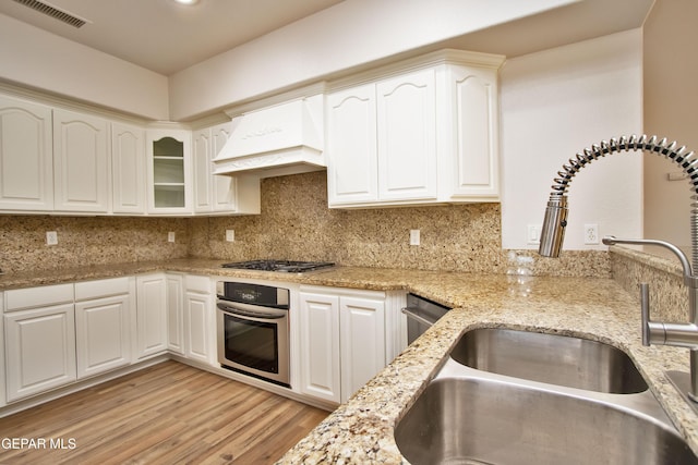 1483 Via Appia St, El Paso, TX 79912 - kitchen featuring appliances with stainless steel finishes, a sink, premium range hood, light wood-style flooring, and light stone counters