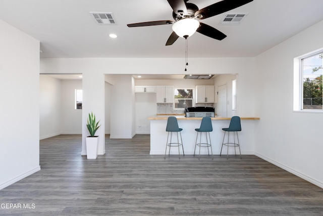 kitchen with white cabinets, a peninsula, ceiling fan, baseboards, and a kitchen breakfast bar