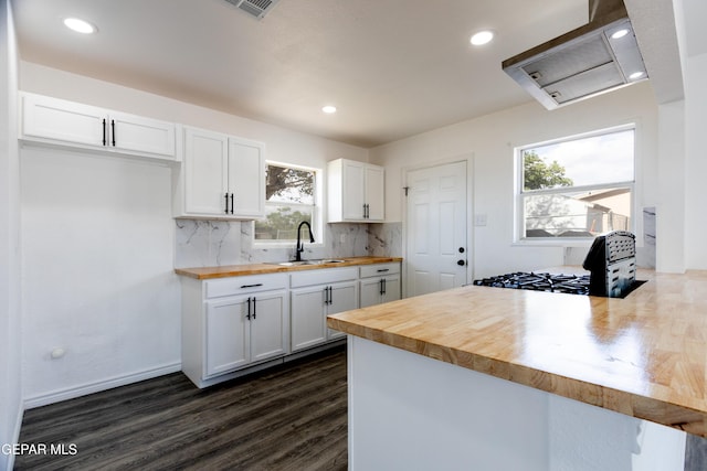 kitchen featuring butcher block counters, a sink, a peninsula, white cabinets, and exhaust hood