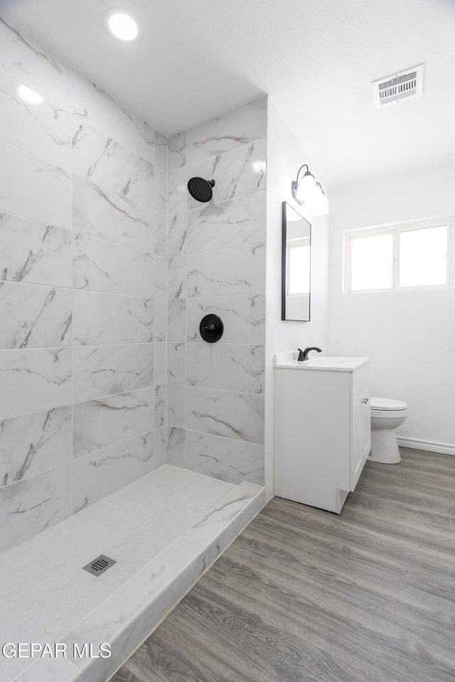bathroom featuring vanity, a tile shower, toilet, baseboards, and recessed lighting