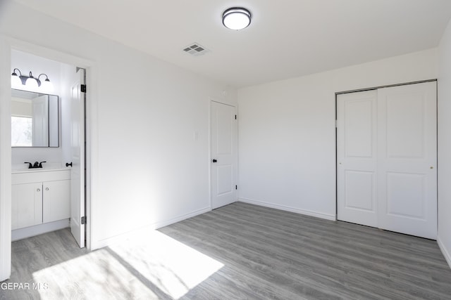 unfurnished bedroom featuring light wood-style floors, a closet, ensuite bathroom, and baseboards