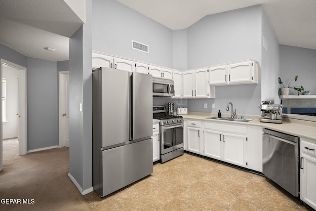 kitchen featuring appliances with stainless steel finishes, a sink, white cabinetry, light countertops, and a high ceiling