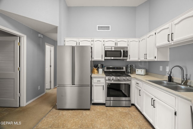 kitchen featuring appliances with stainless steel finishes, a sink, white cabinets, light countertops, and a high ceiling
