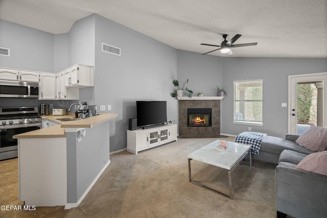 living room featuring a ceiling fan, baseboards, lofted ceiling, a tiled fireplace, and a textured ceiling