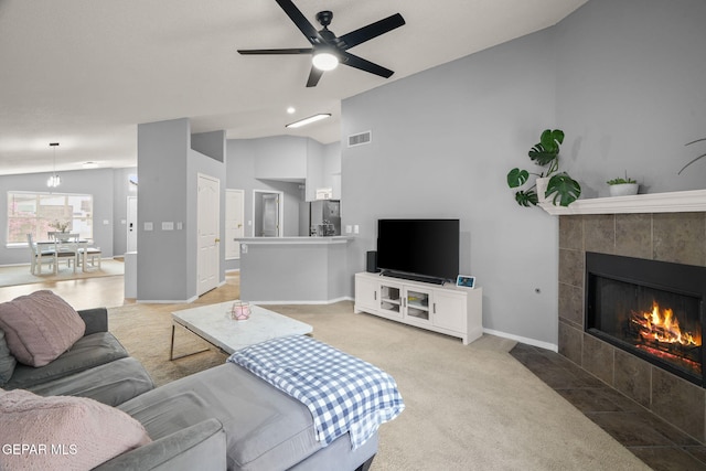 living area featuring vaulted ceiling, ceiling fan, light colored carpet, a fireplace, and baseboards