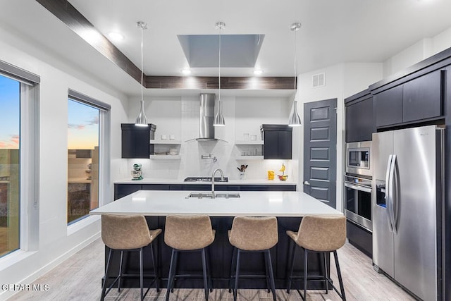 kitchen with stainless steel appliances, wall chimney range hood, light countertops, backsplash, and open shelves