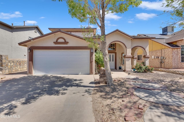 mediterranean / spanish-style house with driveway, a garage, central air condition unit, stucco siding, and solar panels