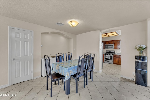 dining area featuring arched walkways, a textured ceiling, baseboards, and light tile patterned flooring