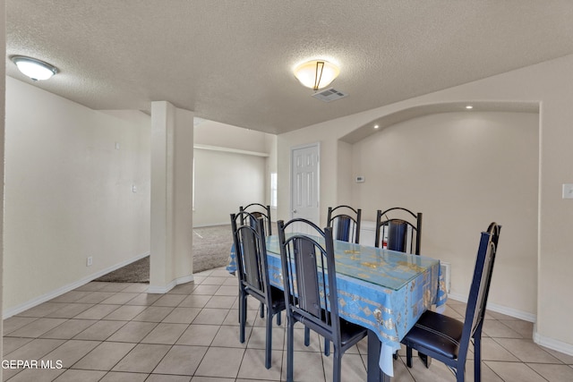 dining space with a textured ceiling, light tile patterned floors, baseboards, and arched walkways