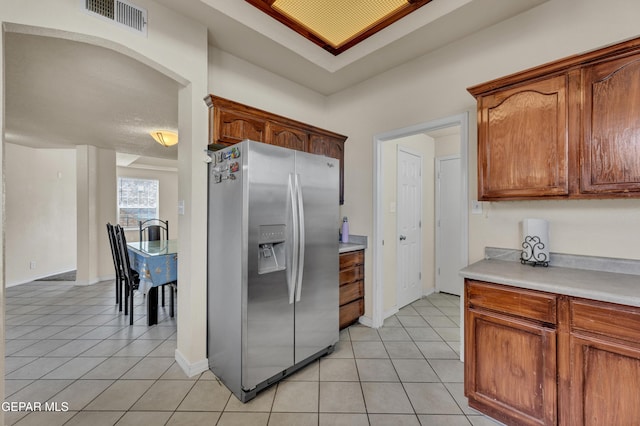 kitchen featuring stainless steel refrigerator with ice dispenser, light tile patterned floors, light countertops, baseboards, and arched walkways