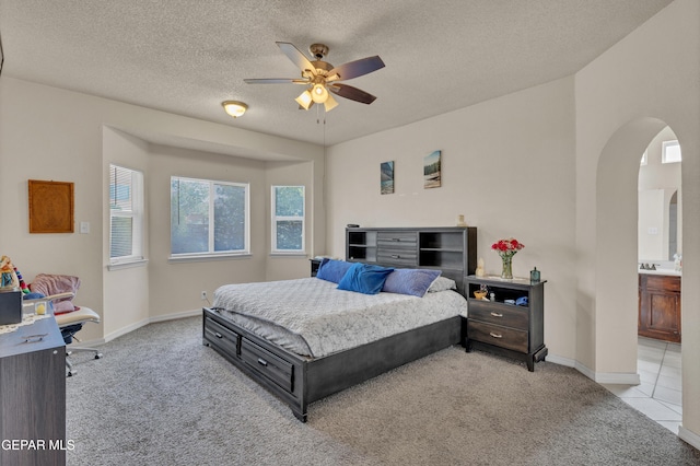 bedroom with light carpet, arched walkways, a textured ceiling, baseboards, and connected bathroom
