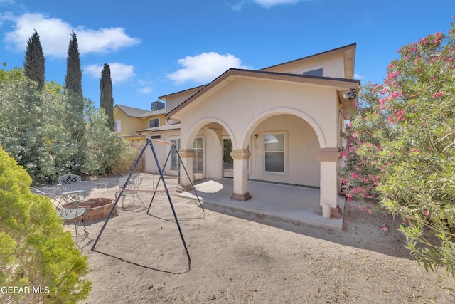 rear view of house with an outdoor fire pit, stucco siding, and a patio