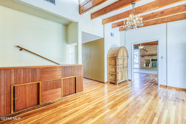 8024 Tonto Pl, El Paso, TX 79904 - unfurnished room with a chandelier, light wood-type flooring, beam ceiling, a brick fireplace, and a towering ceiling