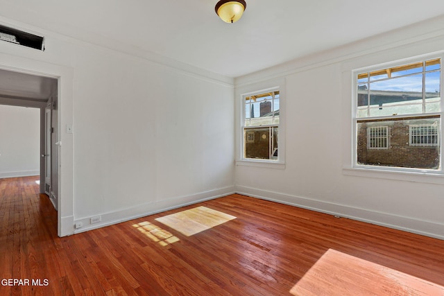 empty room with wood finished floors, healthy amount of natural light, and baseboards