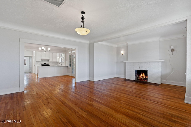 unfurnished living room featuring a brick fireplace, hardwood / wood-style floors, a textured ceiling, a chandelier, and baseboards