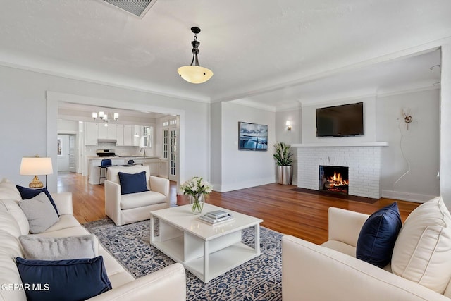living area with light wood-type flooring, a fireplace, a chandelier, baseboards, and crown molding