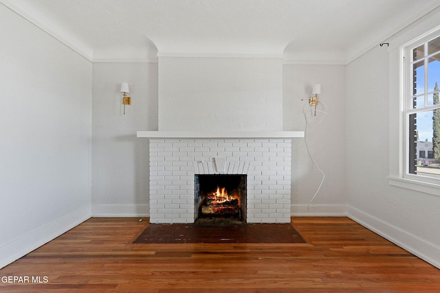 unfurnished living room featuring a fireplace, crown molding, wood finished floors, and baseboards