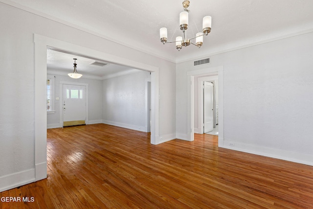 empty room with a chandelier, baseboards, wood finished floors, and crown molding