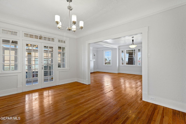 unfurnished dining area featuring a chandelier, wood finished floors, baseboards, and french doors